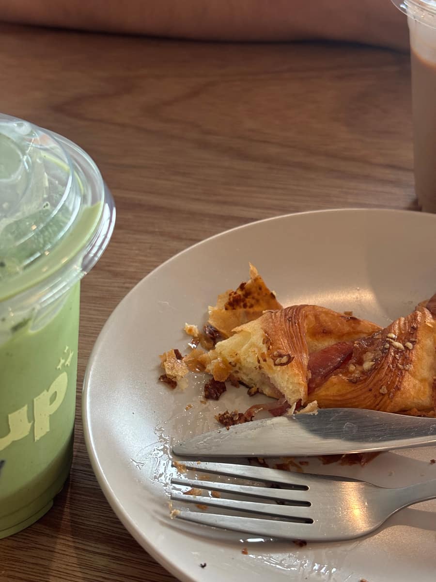 A bacon twist pastry and an iced matcha latte on a wooden table at Citycup BKK