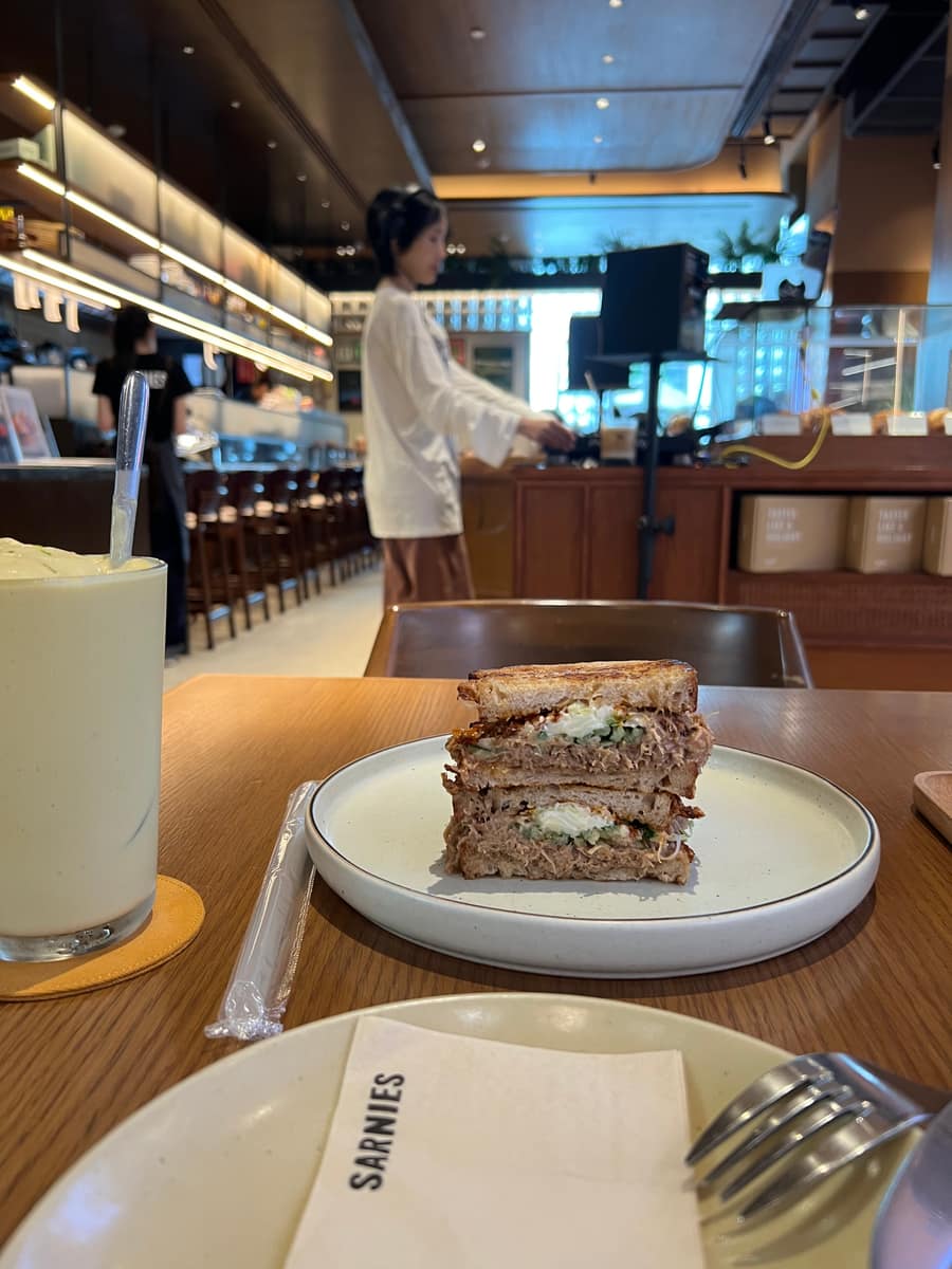 A toasted sandwich on a plate with a Sarnies napkin, the cafe counter behind