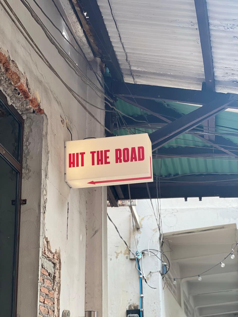 A vintage lightbox sign reading Hit The Road above a doorway on Song Wat Road