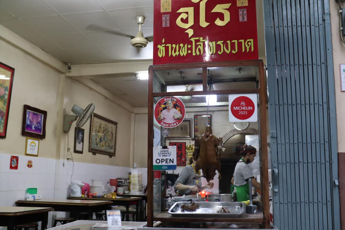 The Urai Han Palo shopfront on Song Wat, a whole braised goose hanging in the glass case beneath a Michelin sticker