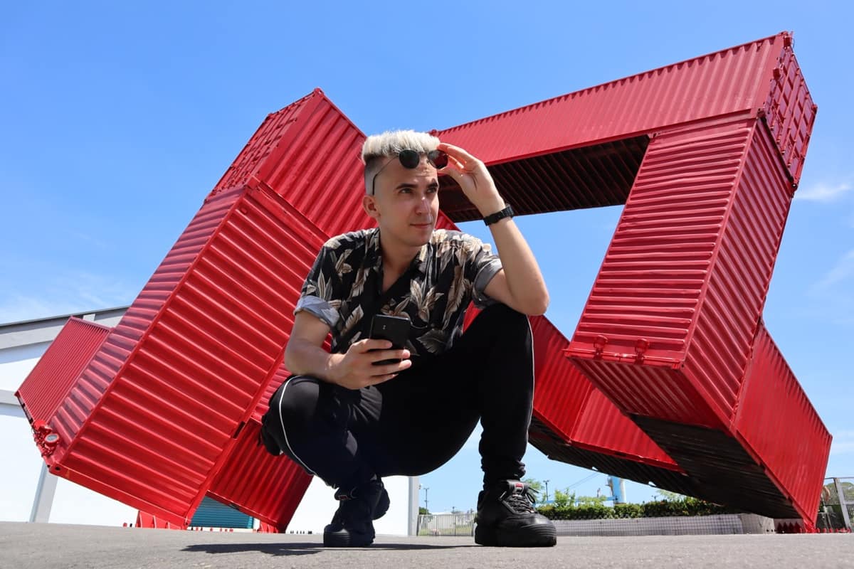 A person crouched beneath a red shipping-container sculpture in Kaohsiung